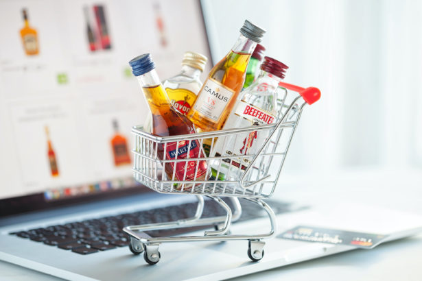 Minsk, Belarus - January 16, 2018: Illustrative editorial photo of shopping cart full of small alcohol bottles - Camus and Martell cognacs, Havana club rum, Beefeater gin on laptop. Minsk, Belarus.